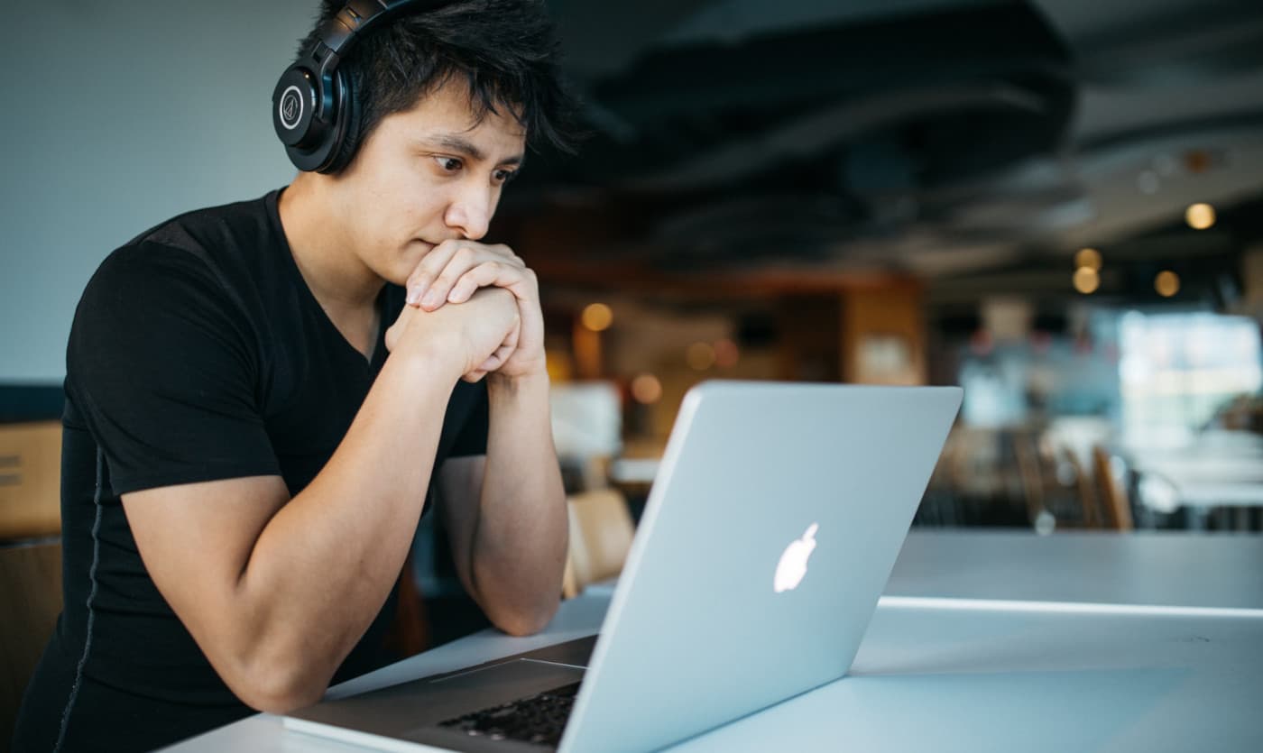 A male with dark hair wearing headphones, loocking into the macbook